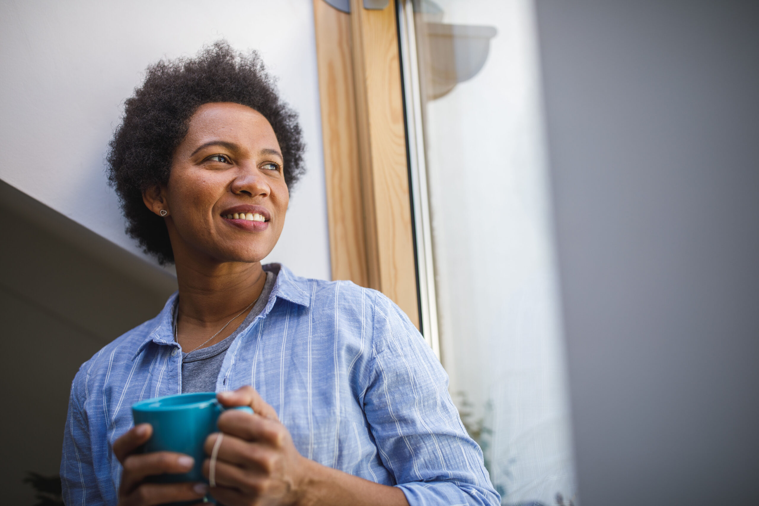 Cheerful mid adult woman enjoying a cup of tea and looking out the window
